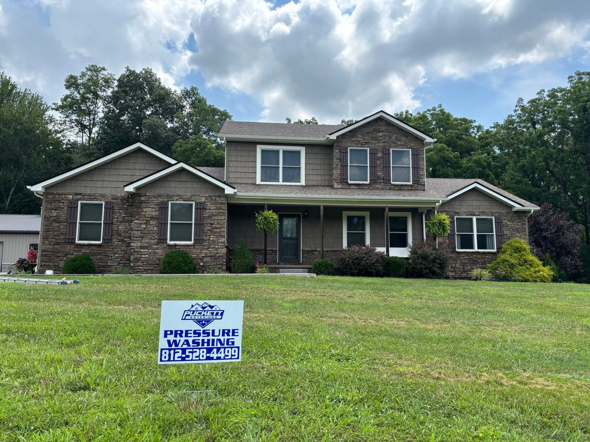 Puckett Exteriors yard sign on the lawn of a stone and cedar-shake two-story home after an exterior wash